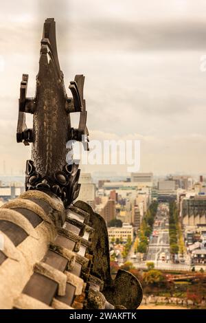 looking out from the upper floor of himeji castle at one of the ornate carved carp roof ornaments with the wide boulevard of otemai street Stock Photo