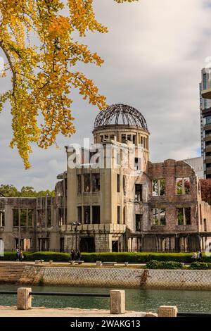 the A-Bomb dome or genbaku dome is a preserved ruin in hiroshima peace memorial park on a sunny day with the colourful autumnal leaves Stock Photo