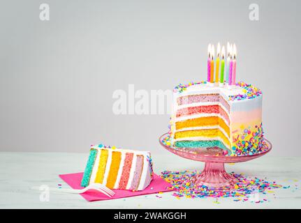 A colorful rainbow layered birthday cake with white icing and a ...