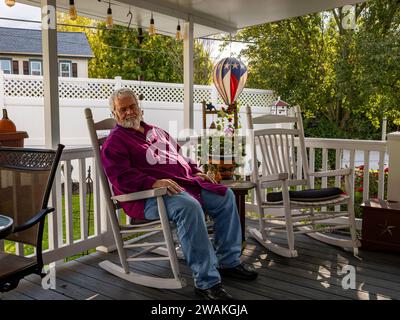 An elderly man resting on a rocking chair on a deck, enjoying his retirement Stock Photo