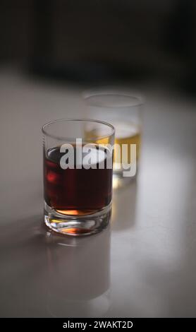 Two small shot glasses filled with red and yellow alcoholic drinks backlit on a white glossy table Stock Photo