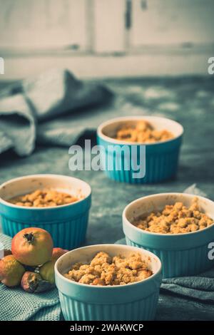 Apple crumble in small blue molds on a rustic gray table, vertical Stock Photo