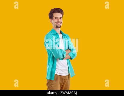 Smiling young man standing with hands crossed on yellow background Stock Photo