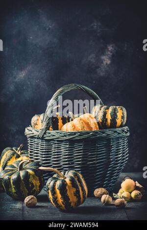 Basket with various small pumpkins with a striped pattern on dark background, vertical with copy space Stock Photo