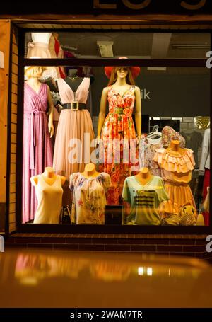 Bunch of headless mannequins show spring clothes collection. Standing dummies in store. Orange T-shirt, white pants, dress, skirt, sweatshirt, blazer, Stock Photo