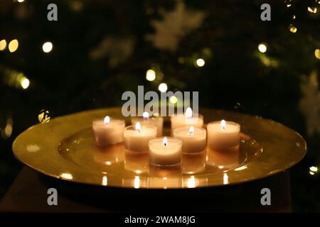 Close-up view of burning tealight candles on a golden plate against a dark Christmas background Stock Photo