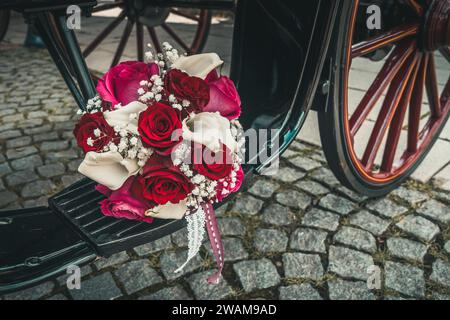Bridal bouquet with red, pink and white roses and white callas on the step of a black carriage Stock Photo
