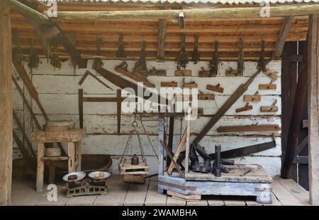 Collection of planers and retro wood saws hang on a wooden wall near an old house. Carpenters plane and other things on the wall Stock Photo