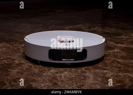A white robot vacuum cleaner on a brown tile Stock Photo