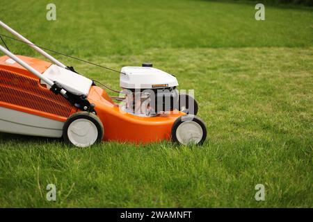 Close up orange-grey electric lawn mower on bright lush green lawn. Gardening work tools. Rotary lawn mower machine cut grass. Professional lawn care Stock Photo