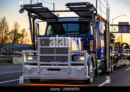 Blue classic industrial car hauler big rig semi truck tractor with turner on lights transporting cars on the modular two level hydraulic semi trailer Stock Photo