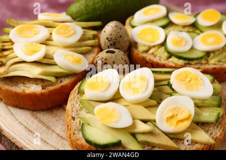 Tasty toasts with quail eggs, avocado and cucumber on table, closeup Stock Photo