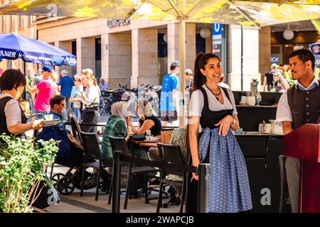 Munich, Germany - July 22, 2023: Street restaurant and waiters in national costumes on square of Marienplatz town hall of Marien Square in Munich, Bavaria, Germany Stock Photo