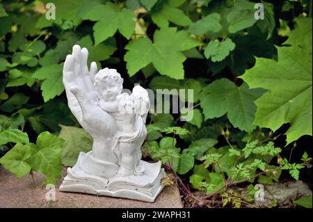 Grave decoration with a white hand and an angel in front of green leaves Stock Photo