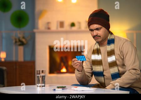 Middle aged sick man in winter wear checking pills prescription or dosage before taking at home - concept of self care, responsibility and wellbeing Stock Photo