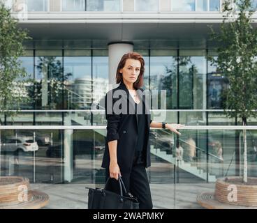 Serious and confident middle-aged woman wearing formal black clothes standing against a modern business building Stock Photo