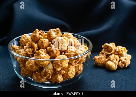 View of sweet caramel almonds in transparent glass bowl on black cloth background. Stock Photo