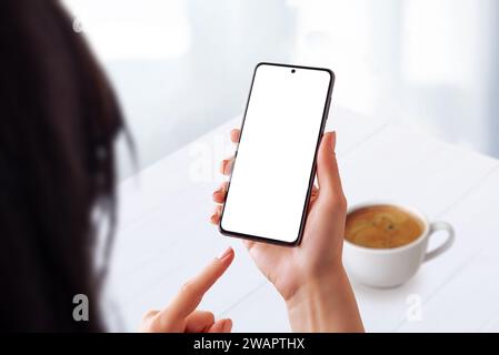 Woman in a coffee shop using a smartphone with an isolated screen for mockup. Ideal for showcasing mobile usability in a casual coffee time setting Stock Photo