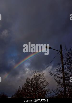 Double rainbow over a street lamp and the top of a leafless tree in a gray-blue cloudy sky Stock Photo