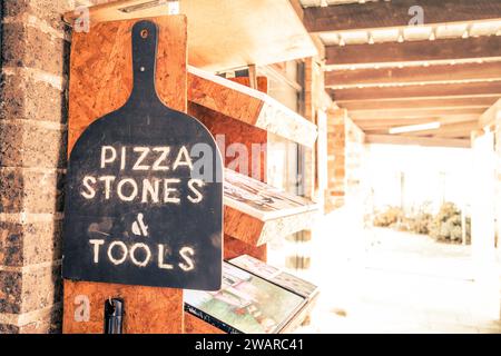 A close up image of a pizza paddle leaning against a brick wall with a bookshelf in the background Stock Photo