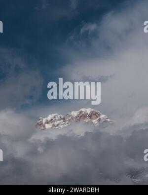 A snow-capped mountain is silhouetted against a backdrop of clear blue sky and wispy white clouds Stock Photo