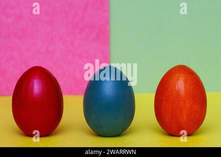 Two red and one blue handmade decorative eggs on a yellow, blue and purple background. Hand painted eggs on an abstract colorful background. Easter co Stock Photo