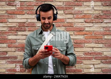 Caucasian man smiling while using phone to send online messages and listen music. Stock Photo
