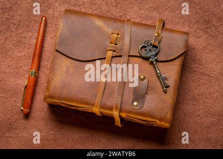 retro leather-bound journal with a decorative key and a luxurt pen on a handmade bark paper, journaling concept Stock Photo