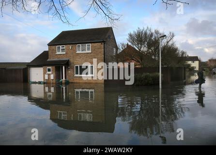 Brampton, UK. 06th Jan, 2024. A resident with a bag and an umbrella wades through flood water as he leaves his home for somewhere safer. Flood alerts remain in place as waters continue to rise in the east of England following storm Henk. Main rivers the River Great Ouse and the River Nene have burst their banks and spilled onto the surrounding countryside and with drains full to capacity they are backing up in residential areas. Credit: SOPA Images Limited/Alamy Live News Stock Photo