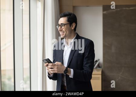 Cheerful young Arab entrepreneur man holding mobile phone Stock Photo