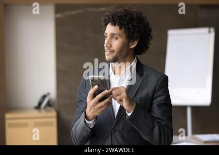 Thoughtful young business leader man holding mobile phone Stock Photo