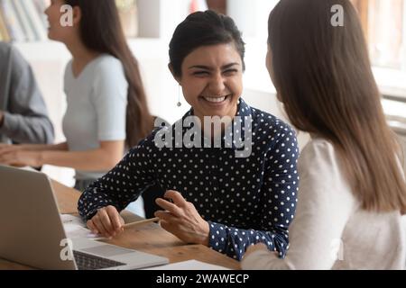 Overjoyed multiethnic female students laugh cooperating at project Stock Photo