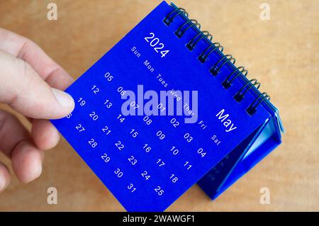 Hand showing May 2024 table calendar on wooden background. Calendar concept. Stock Photo