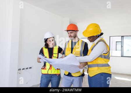Group of professional construction workers engineers team meeting standing together work in new house construction site with floor plan. Stock Photo