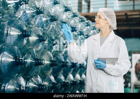 women worker working in drinking water plant factory checking count water bottle gallon in warehouse with hygiene uniform. Stock Photo