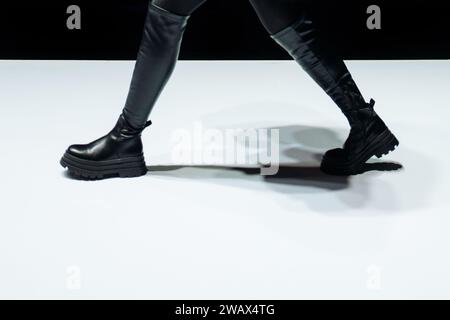 Female legs in black leather boots walking on the white floor Stock Photo