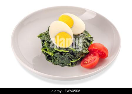 Spinach cooked with cut hard boiled egg and cut cherry tomato in white dish isolated on white with clipping path included Stock Photo