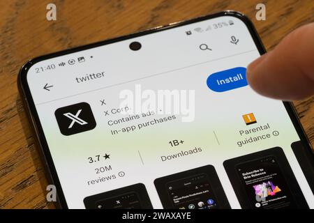 A finger pointing at the the X App (formerly twitter) installation page on a smartphone screen by the American Company X Corp, UK Stock Photo