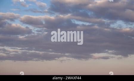 The image shows fluffy clouds against a soft blue sky during sunset. Stock Photo