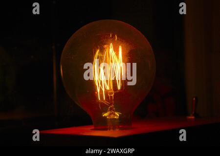 A close up photo of a red and yellow Edison looking light bulb in the dark. Stock Photo