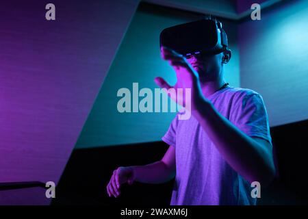 Young man interacting in a digital world, using virtual reality headset with motion tracking tech, making hand gestures in the air. Stock Photo