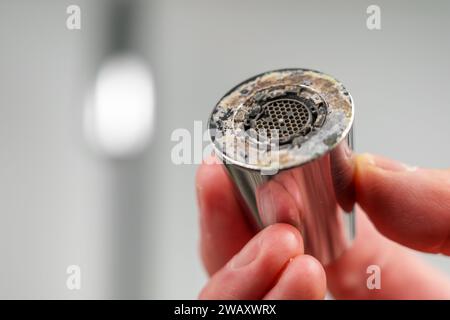 A plumber is holding a chrome faucet aerator with lime scale in kitchen room Stock Photo
