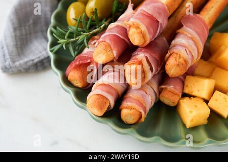 Slices of prosciutto or jamon. Delicious grissini sticks with prosciutto, cheese, rosemary, olives on green plate on dark background. Appetizers table Stock Photo
