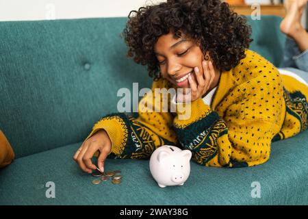 Saving money investment for future. African American girl putting money coin in pink piggy bank. Saving investment budget business wealth retirement financial money banking concept Stock Photo