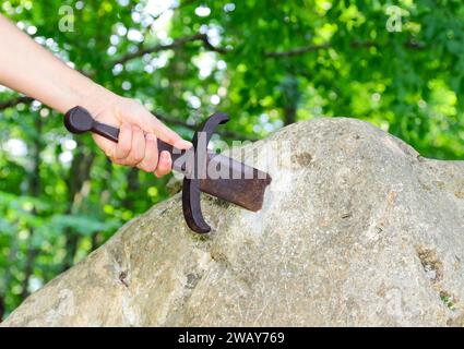 hand of the knight who tries to extract the Excalibur Sword stuck in the rock Stock Photo