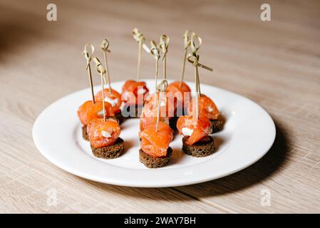 Elegant smoked salmon rolls with cream cheese on dark rye bread, garnished with herbs, served on a white plate. Stock Photo