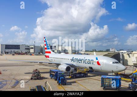 View of parked American Airlines aircraft at airport connected to jet bridge for passenger boarding and with luggage being loaded into cargo Stock Photo