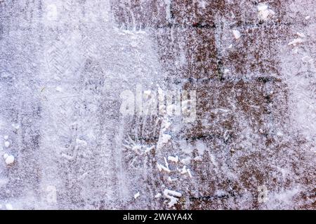 Close-up view of the texture of snow-covered sidewalk tiles with footprints. Stock Photo