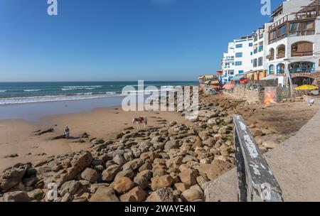 Beachfront buildings on coastal path, with Atlantic Ocean and sandy beach - Taghazout, Morocco Stock Photo