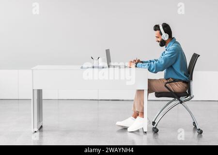 Indian man focused on work with headphones at minimal desk Stock Photo